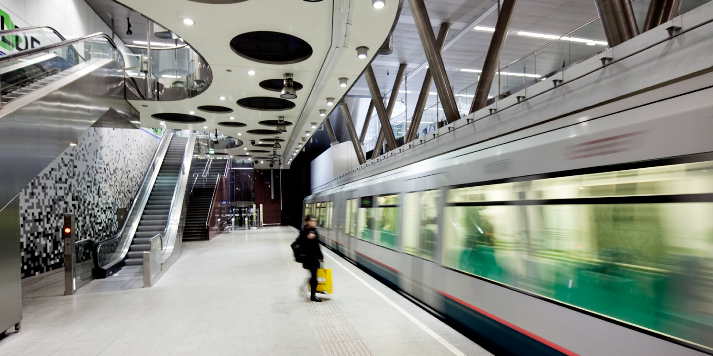 Metrostation Wilhelminaplein met aankomende metro en reiziger op perron, gefotografeerd door E. Fecken, in een moderne en lichte omgeving.